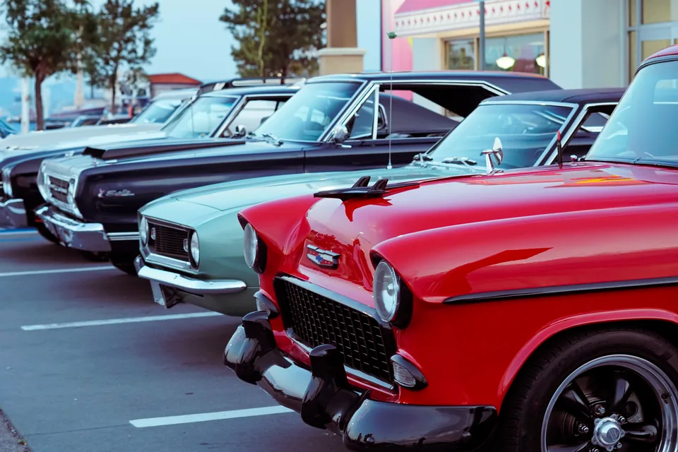 A line of classic cars led by a vivid red Chevrolet