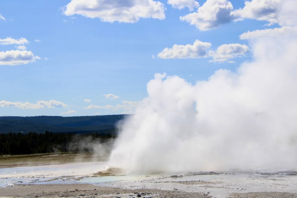 A white geyser plume rising beneath a blue sky
