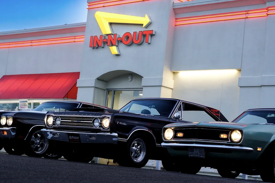 Two black classic cars parked beneath the In-N-Out sign